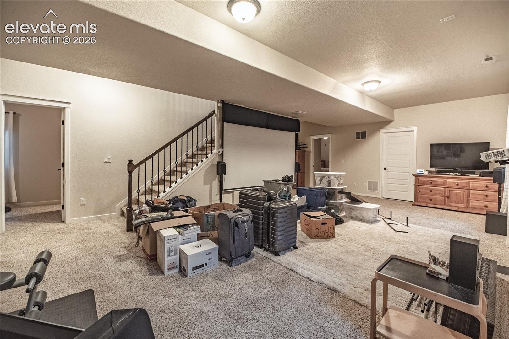 Open-concept interior featuring wall-to-wall carpeting, a staircase with decorative metal balusters, and a retractable ceiling-mounted projector screen
