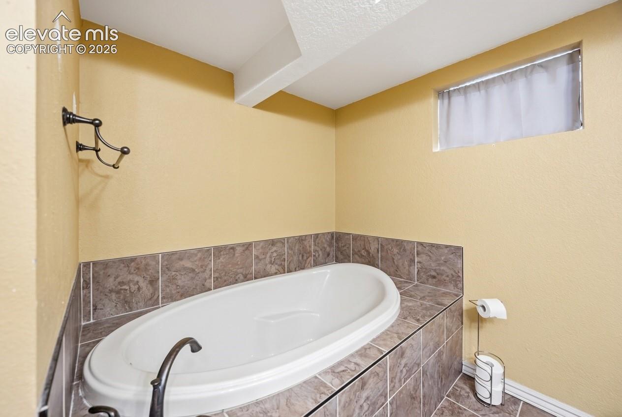 Built-in soaking tub with a dark tile surround and coordinating tile flooring