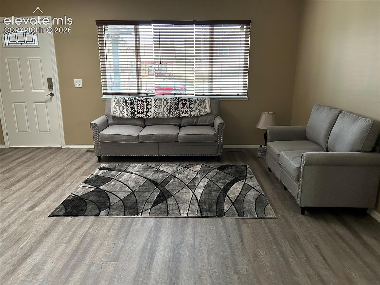 Living area featuring wood-finish flooring, a multi-pane glass insert entry door, and a large window with horizontal blinds