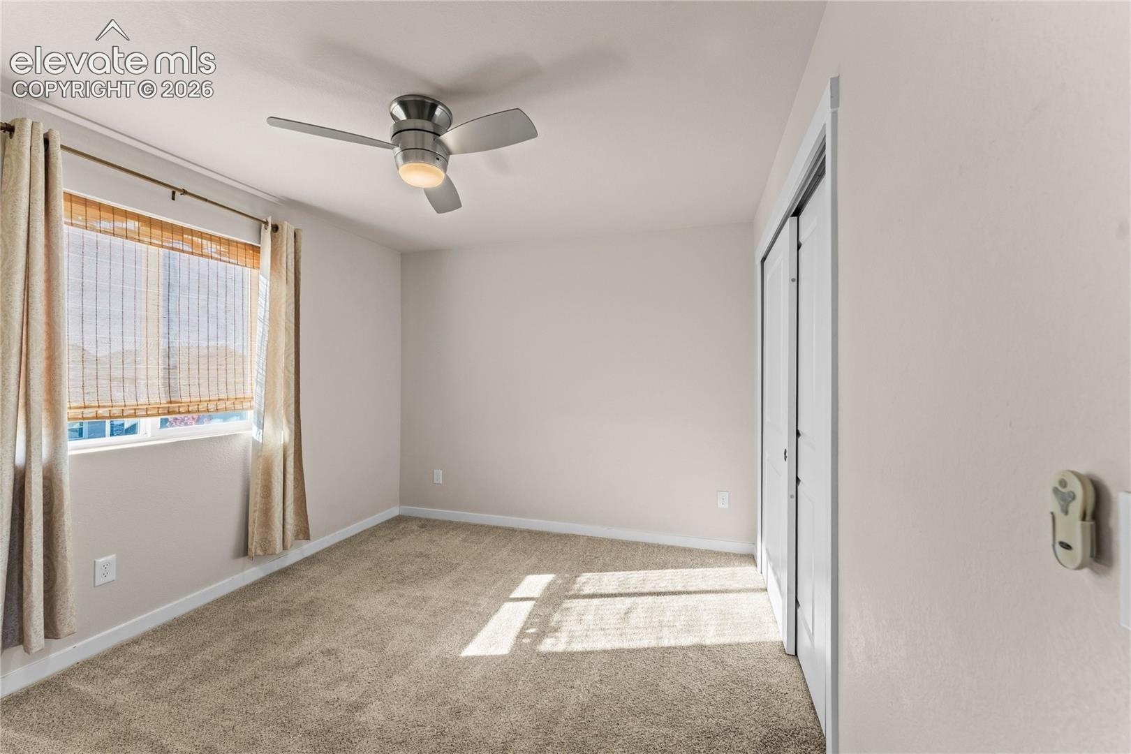Neutral carpeting, ceiling fan with integrated lighting, and sliding closet doors