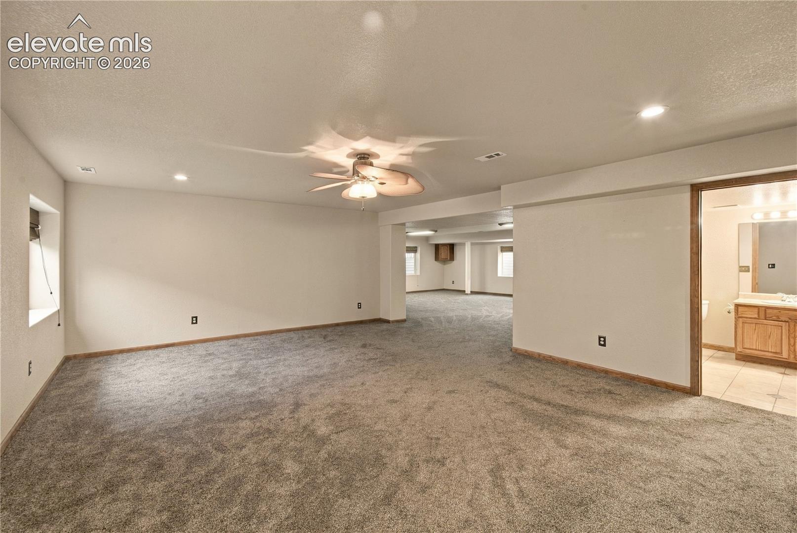 Open-concept interior featuring wall-to-wall carpeting, recessed lighting, ceiling fan with integrated lighting, and a bathroom with a wood-finish vanity