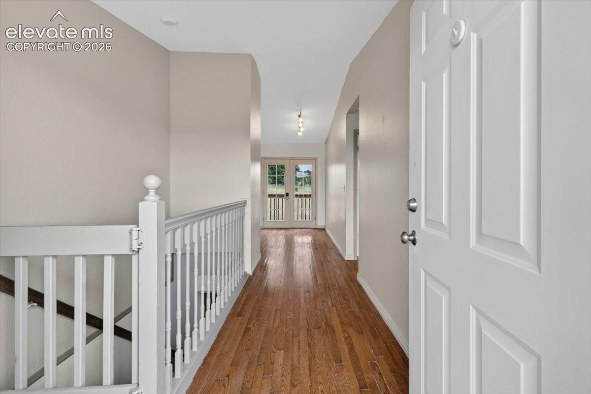 Interior hallway featuring wood-finish flooring, white spindle railing, and double French doors with multi-pane glass