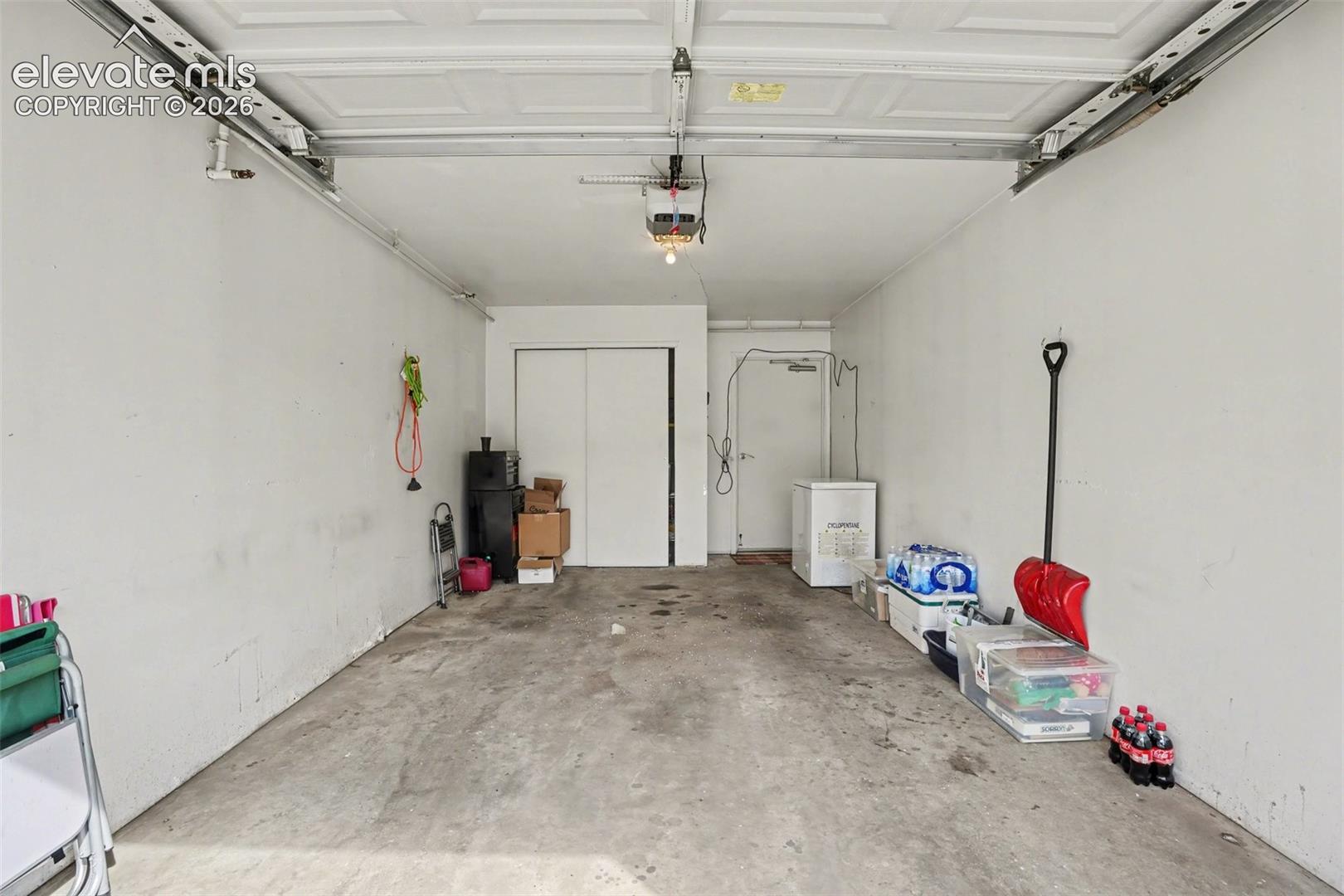Garage featuring a sectional overhead door, automatic door opener, concrete flooring, and built-in closet storage