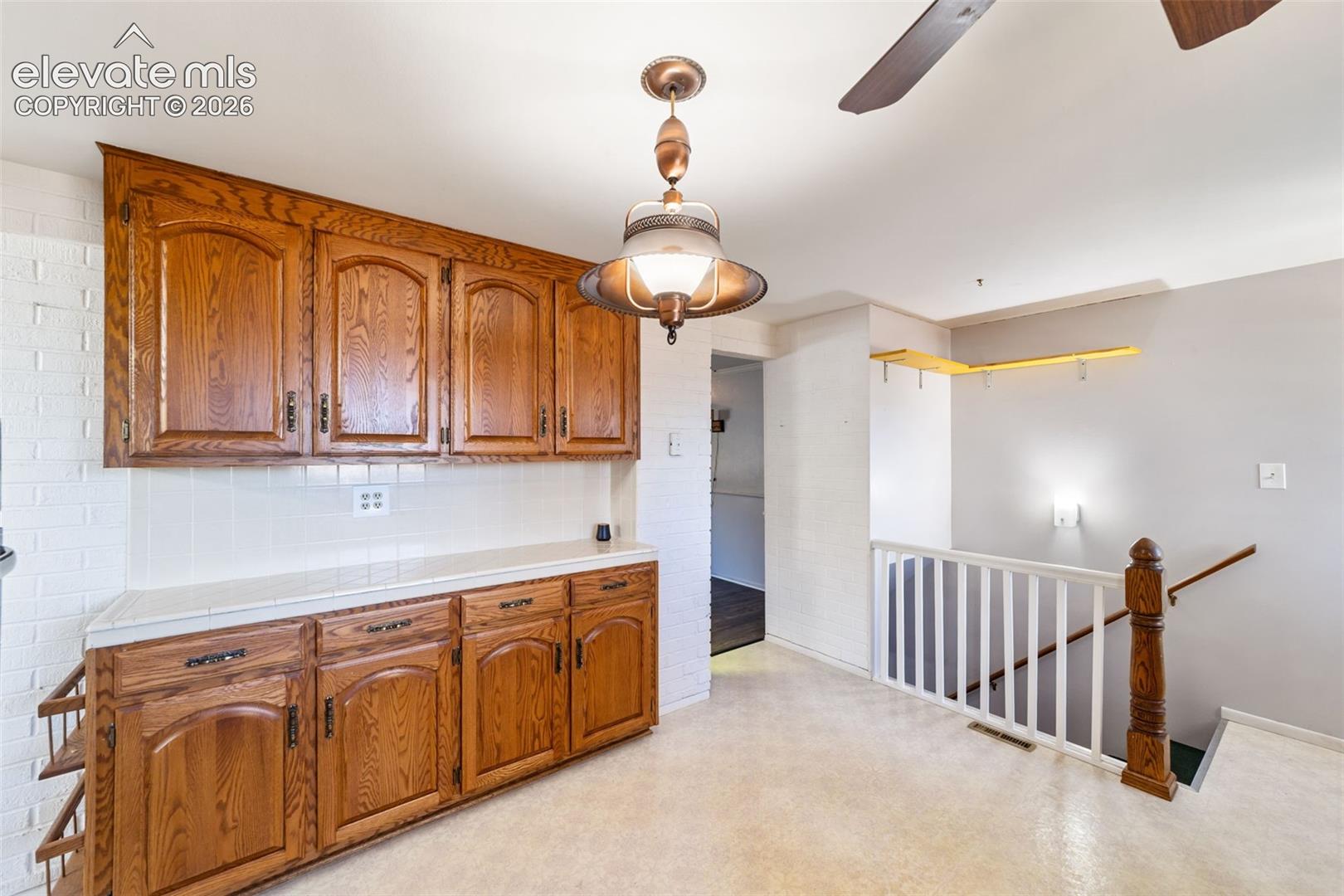 Wood-finish cabinetry with white tile backsplash and light-toned countertops