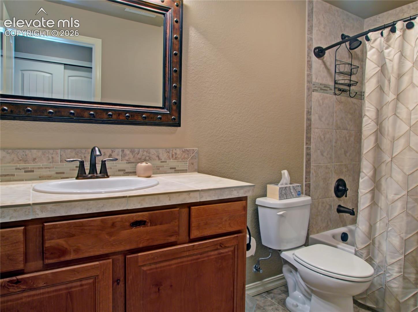 Lower level Bathroom vanity with one sink, full bath tub ,tile countertop, and wood-finish cabinetry