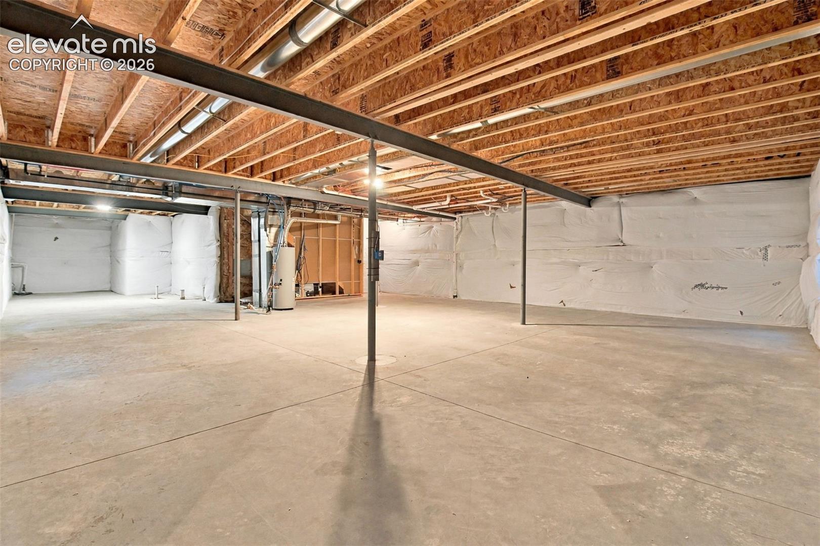 Unfinished lower level featuring concrete flooring, exposed wood joists, steel support beams, and white vapor barrier wall insulation