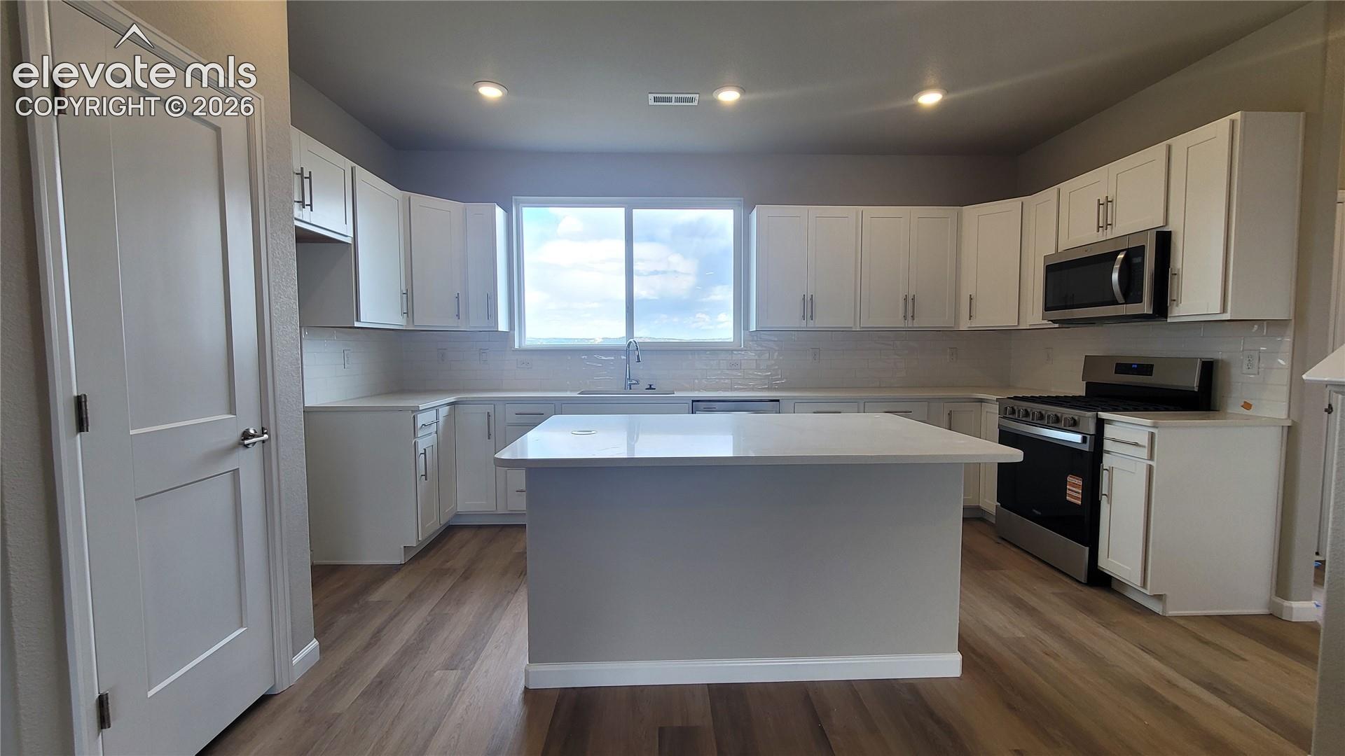 Kitchen with quartz countertops, plenty of cabinets, pantry, island providing additional seating, and stainless steel gas range, microwave, and dishwasher! 