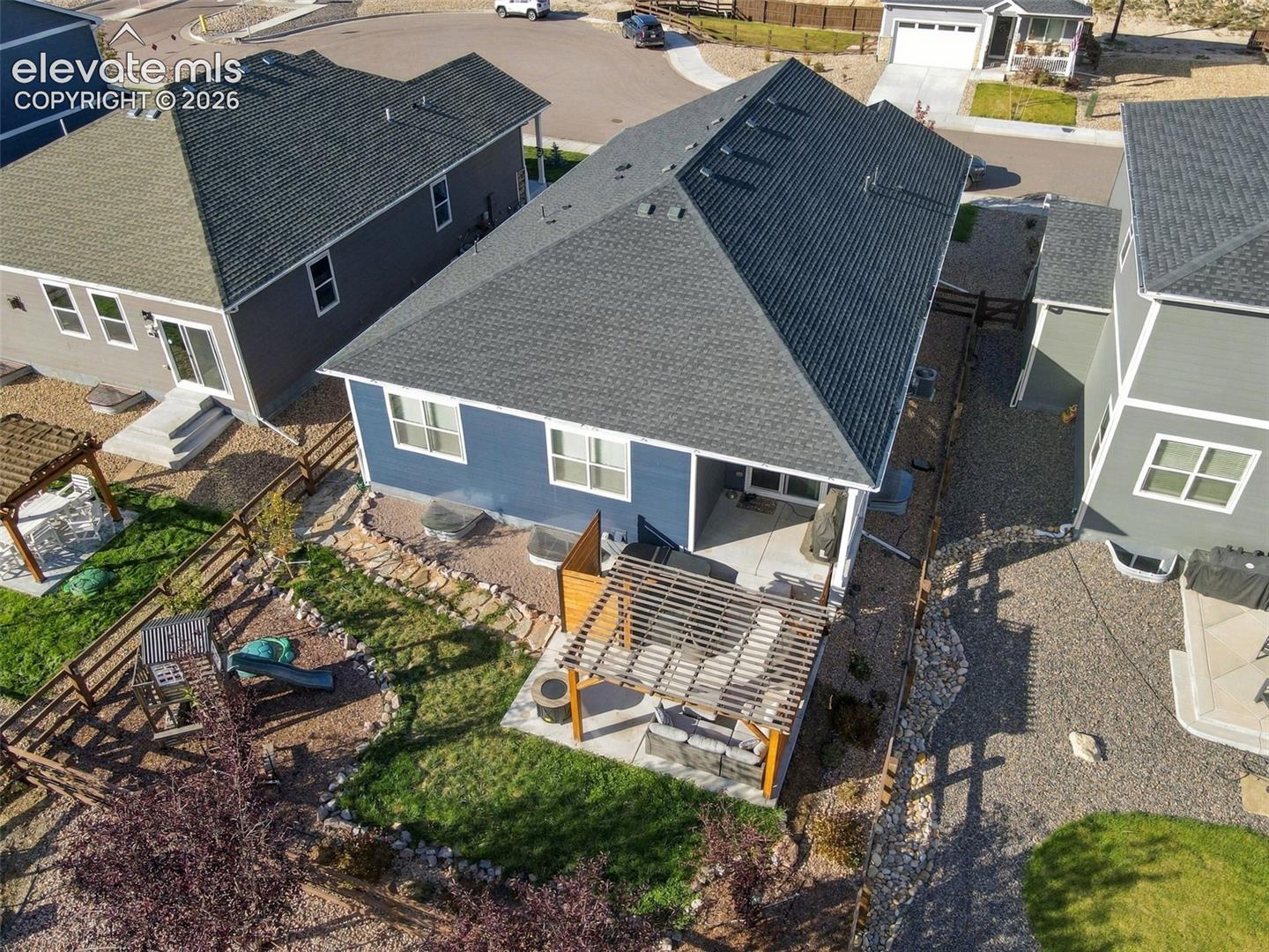 Rear exterior featuring a covered concrete patio, an attached wood-slat pergola, a fenced backyard, and a landscaped area with stone borders