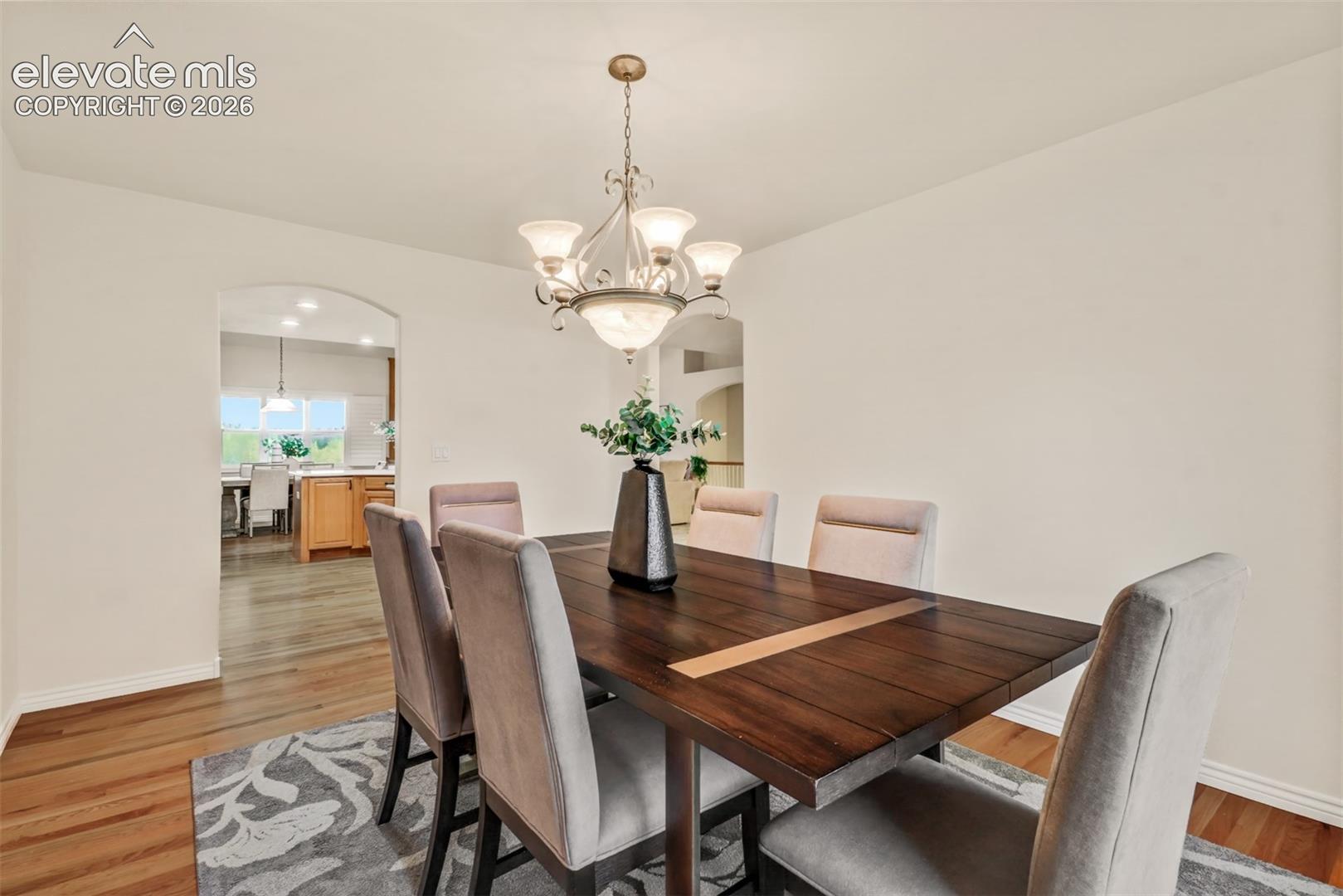 Formal dining area featuring wood-finish flooring, a decorative multi-arm chandelier, and an arched entryway