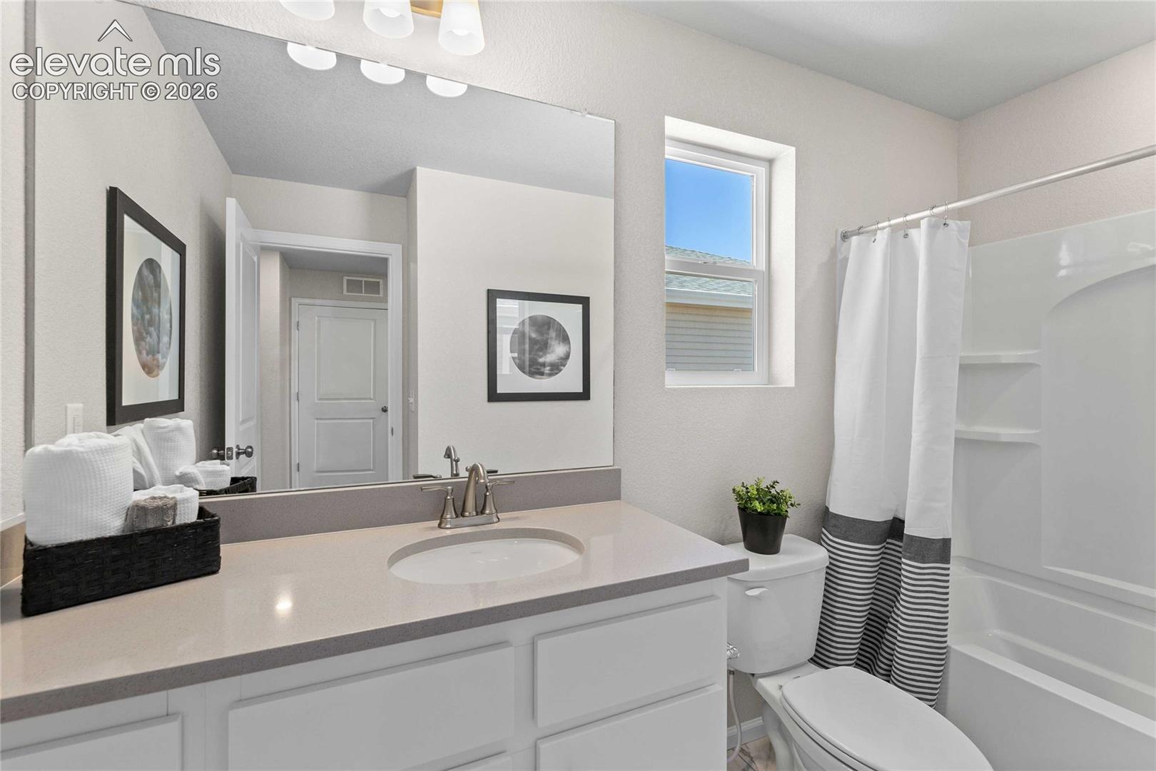 Bathroom featuring a white vanity with a neutral solid-surface countertop, an integrated oval sink, a large wall-mounted mirror, and a tub-shower combination with a surround
*photos of a model home*