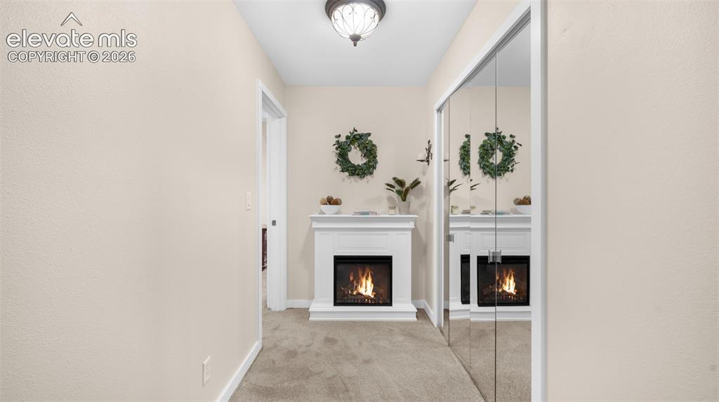 Hallway featuring a built-in electric fireplace with a white mantel, mirrored closet doors, and neutral carpeting