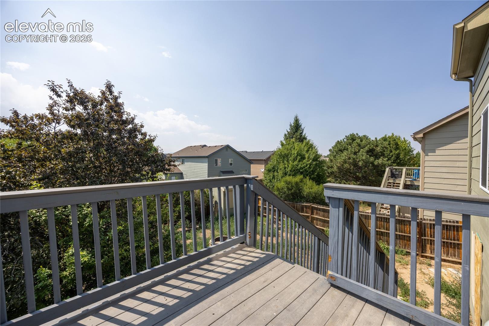 Elevated wood deck with baluster railing, offering exterior access and surrounding landscaping