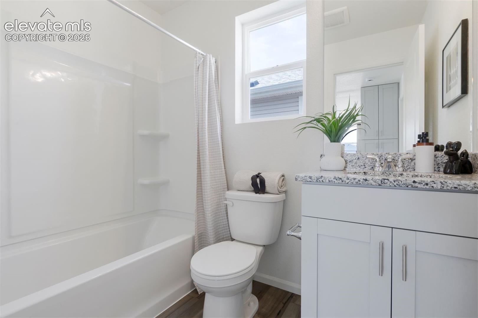 Bathroom with a white tub-shower combination, single vanity with a patterned countertop, and wood-finish flooring
*photos of a model home*