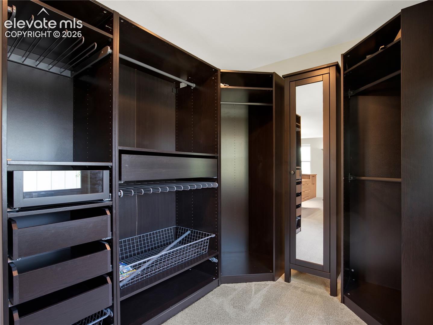 Custom dark wood cabinetry featuring adjustable shelving, multiple pull-out drawers, built-in wire baskets, integrated hanging rods, and an inset full-length mirror