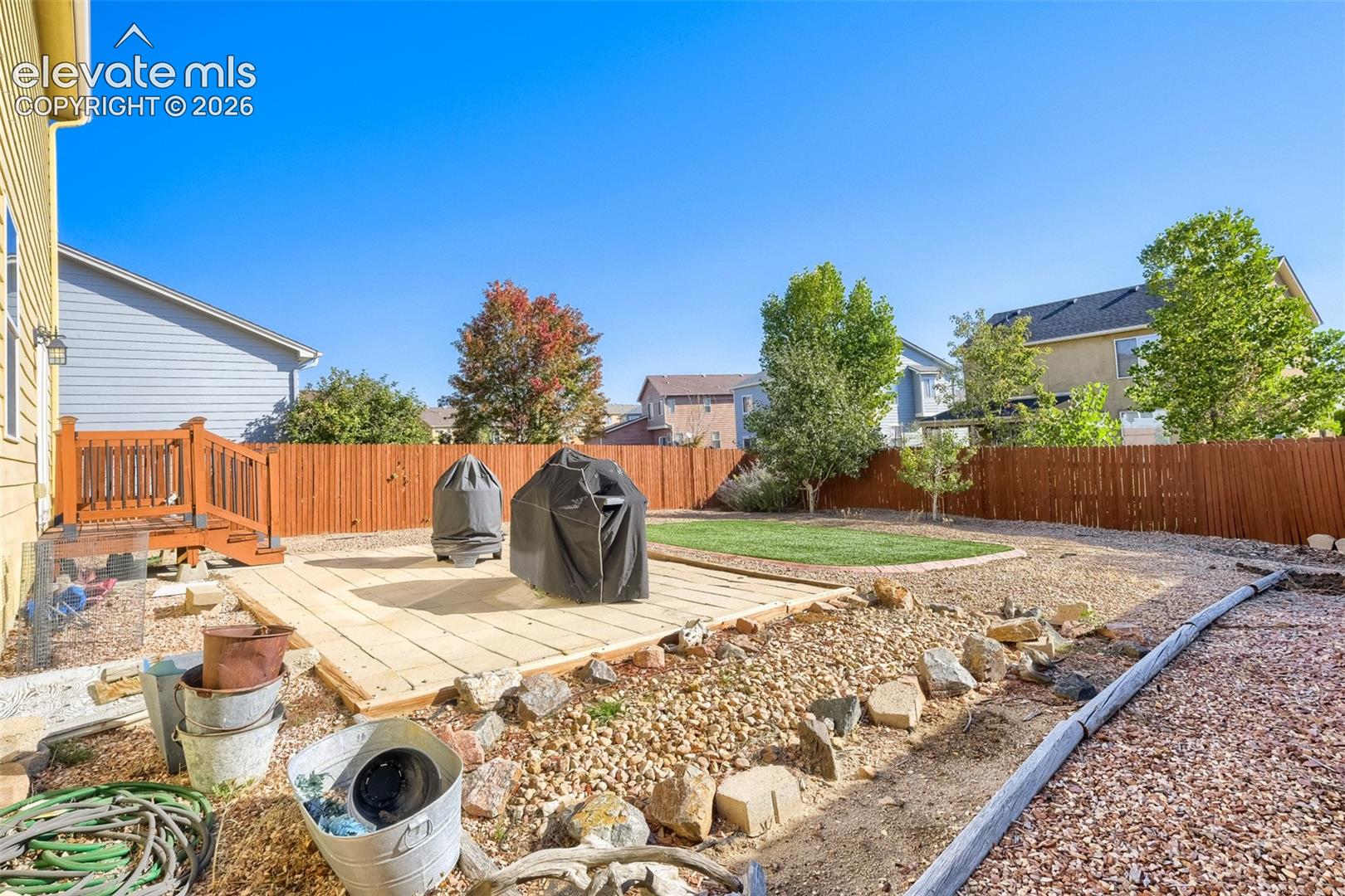 Expansive backyard featuring a wood-plank patio, wooden deck, full privacy fence, and a manicured lawn area