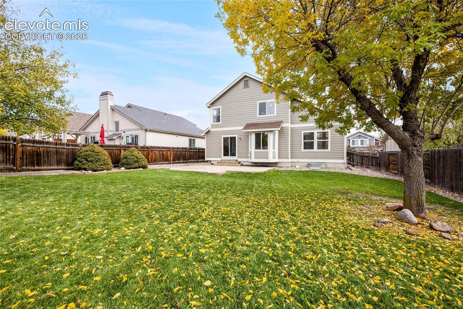 Expansive backyard featuring a manicured lawn, concrete patio, perimeter wood fencing, and mature trees
