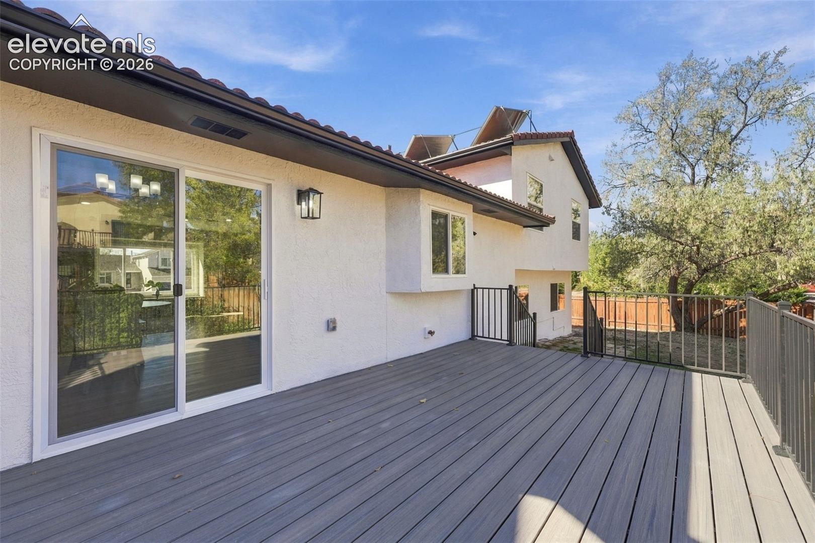 Stucco exterior siding featuring a composite deck, black metal railing, sliding glass door, and roof-mounted solar panels