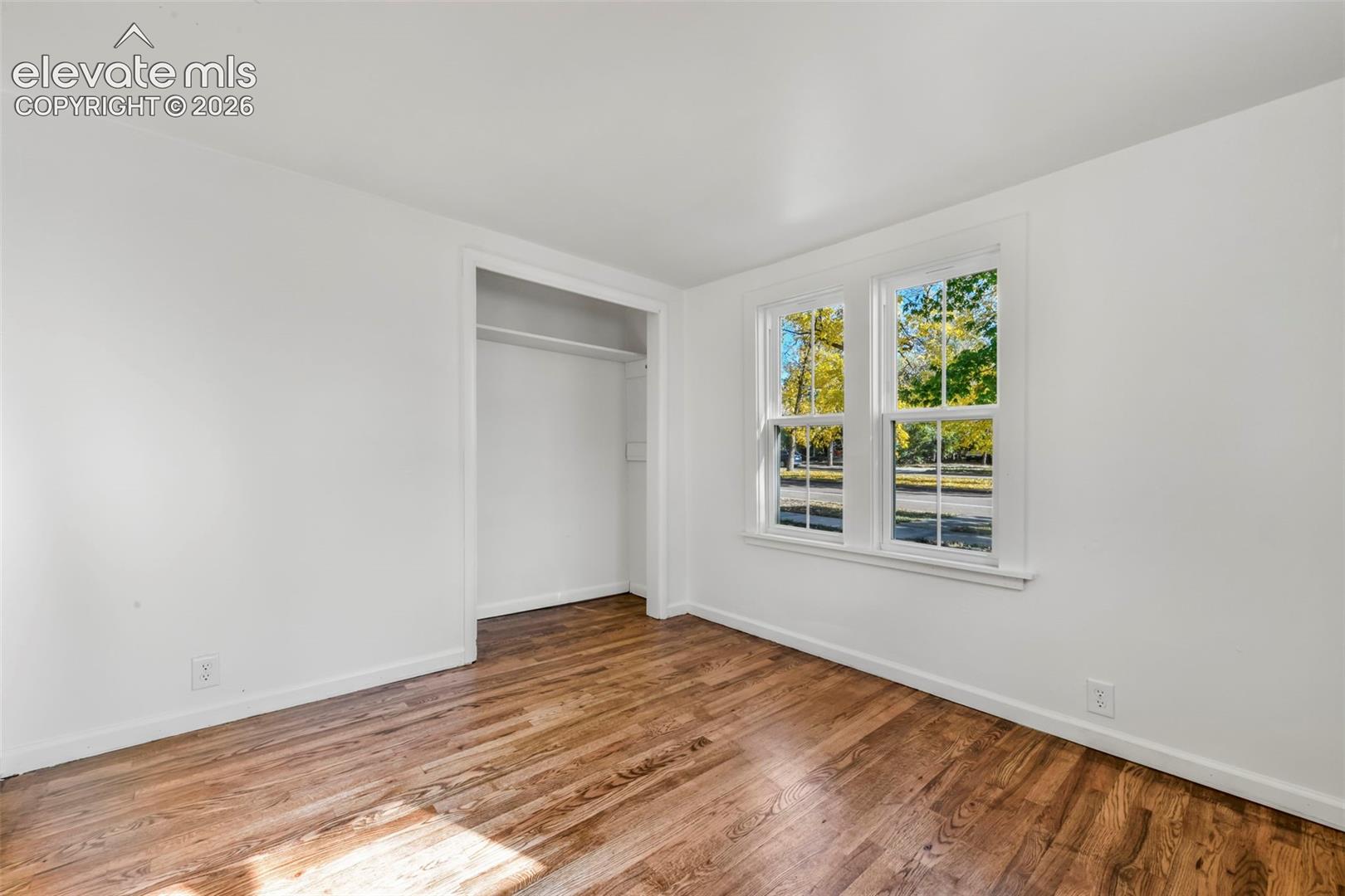 Room featuring wood-finish flooring, white walls, double-hung windows, and a recessed closet with built-in shelving