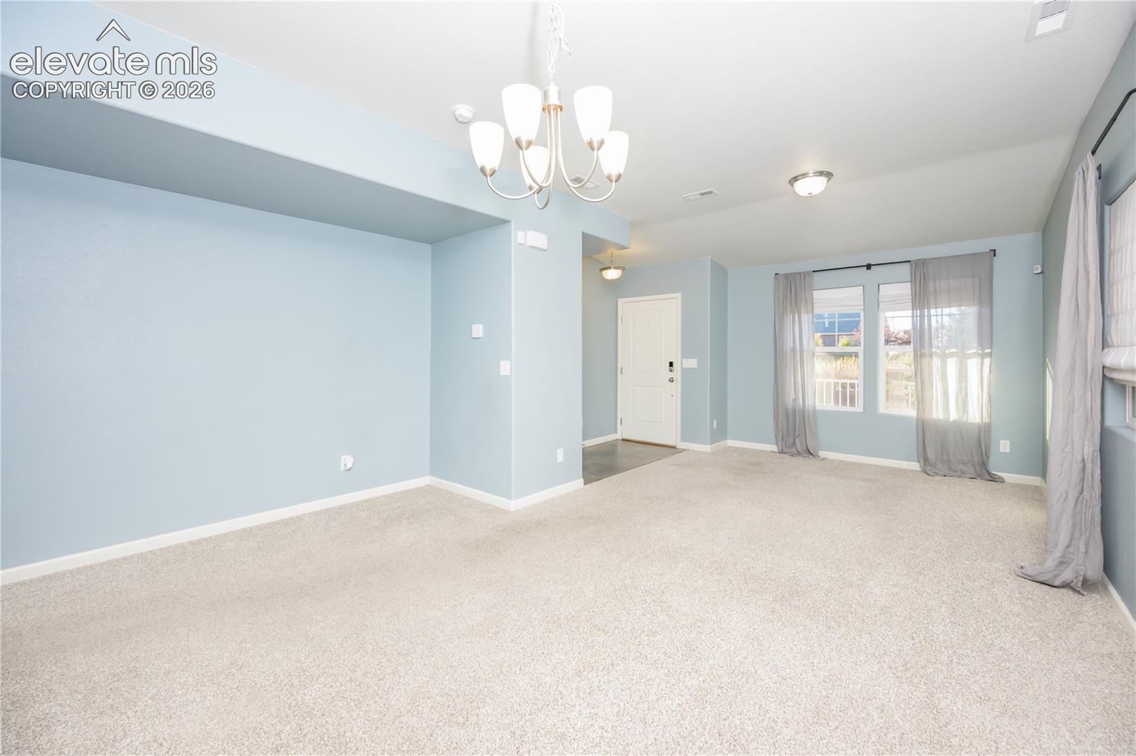 Open-concept area featuring a five-arm multi-light chandelier, neutral wall-to-wall carpeting, recessed lighting, and multiple windows