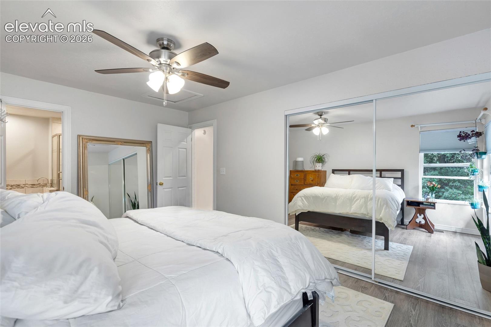 Room featuring light gray walls, wood-finish flooring, a ceiling fan with integrated lighting, and a mirrored sliding closet door