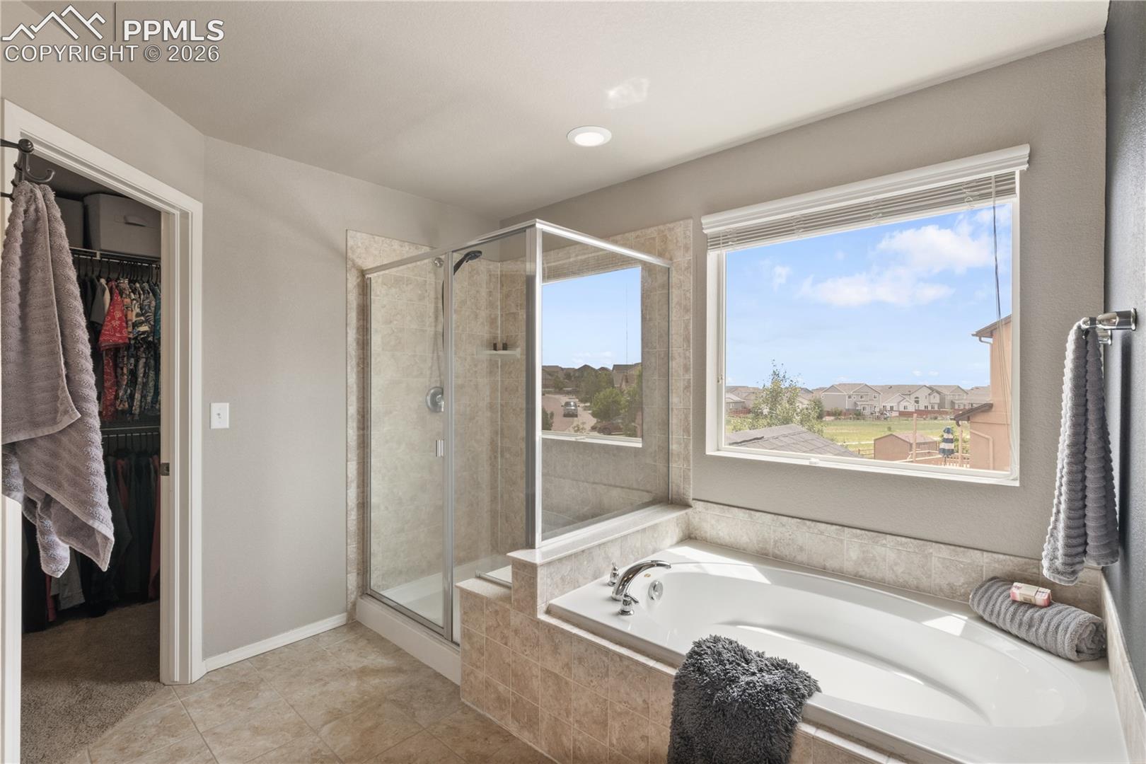 Full bath with a walk in closet, a stall shower, a bath, and light tile patterned floors