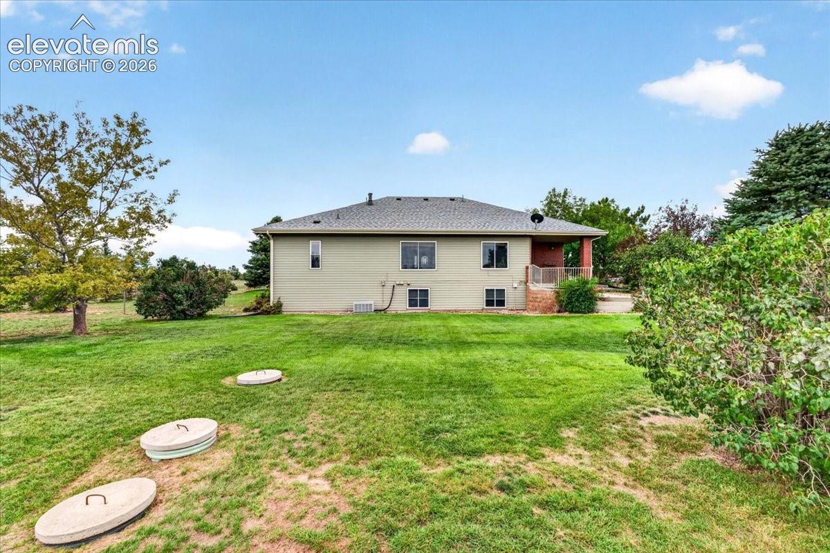 Spacious backyard featuring a manicured lawn, mature trees, and a covered patio with metal railings