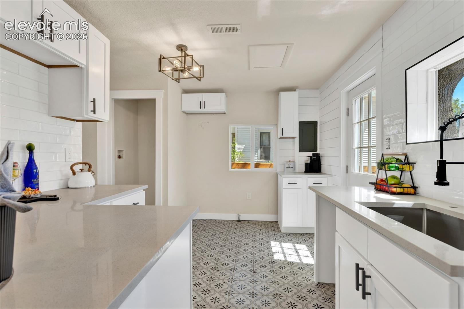Kitchen featuring white shaker-style cabinetry with matte black hardware, light-toned countertops, subway tile backsplash, patterned floor tile, and a farmhouse-style sink with a black pull-down faucet