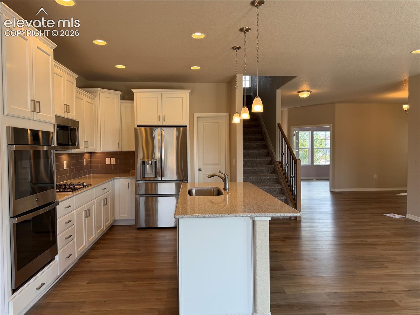 Kitchen with white cabinetry, stainless steel appliances, and an island featuring a sink and pendant lighting