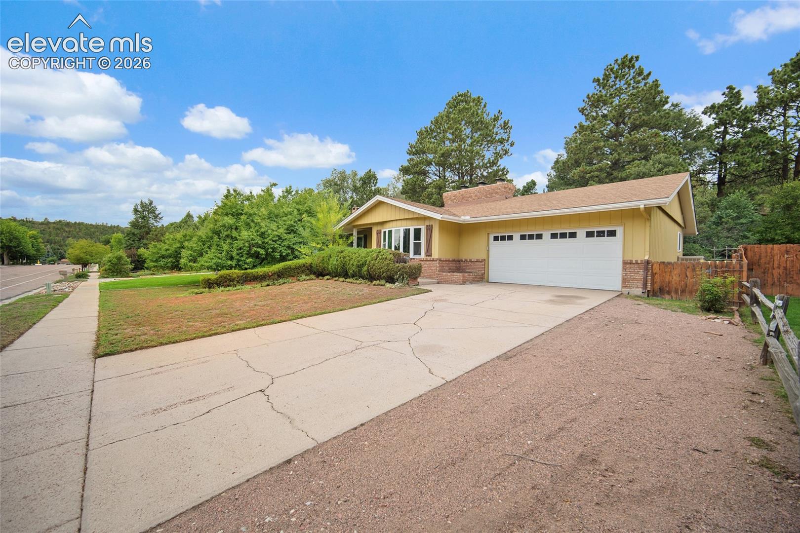 Single-level ranch residence featuring yellow vertical siding, brick accents, a multi-pane bay window, an attached two-car garage, and a concrete driveway