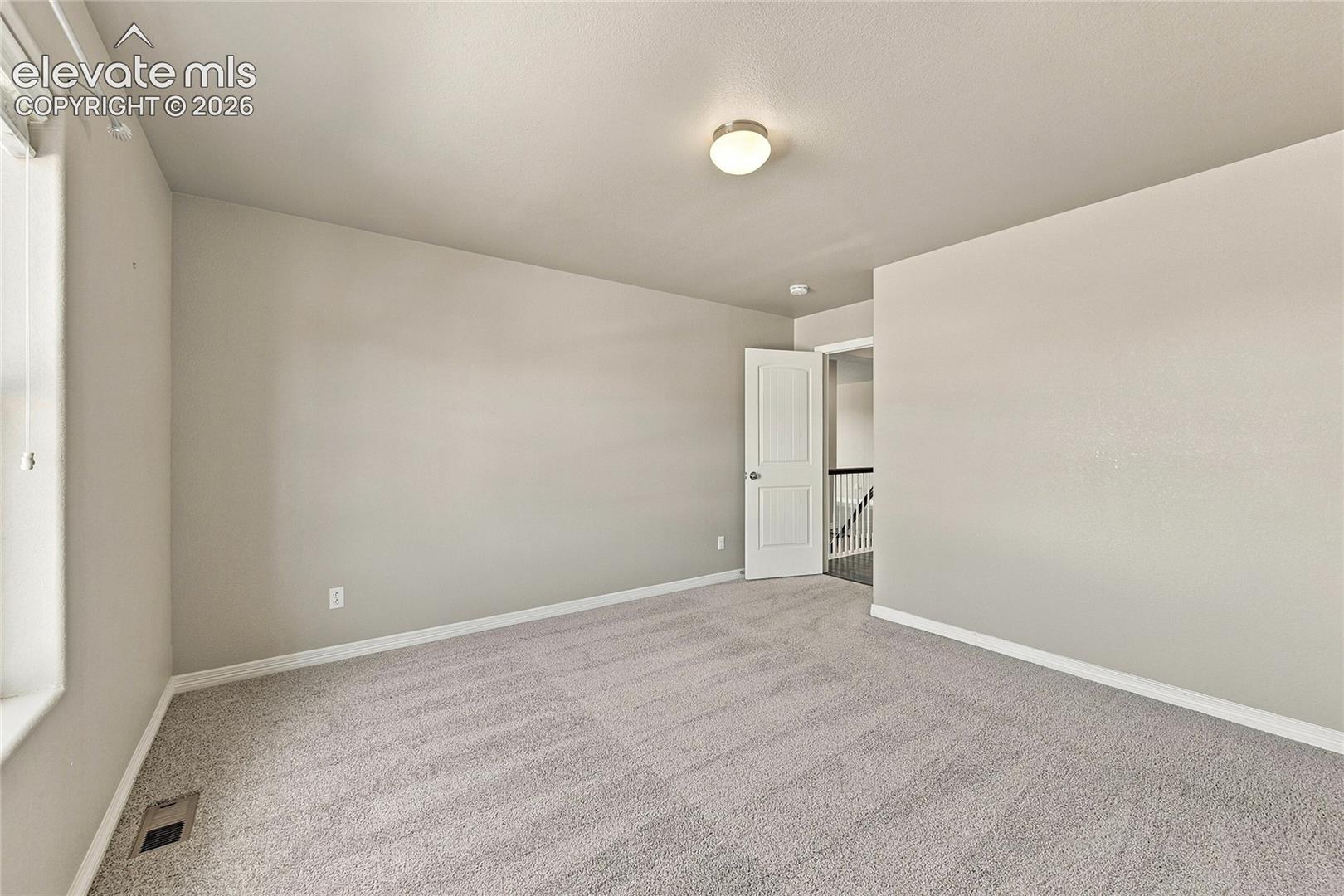 Neutral-toned interior space featuring textured carpeting, smooth-finish walls, a single-panel interior door, and a flush-mount ceiling light fixture