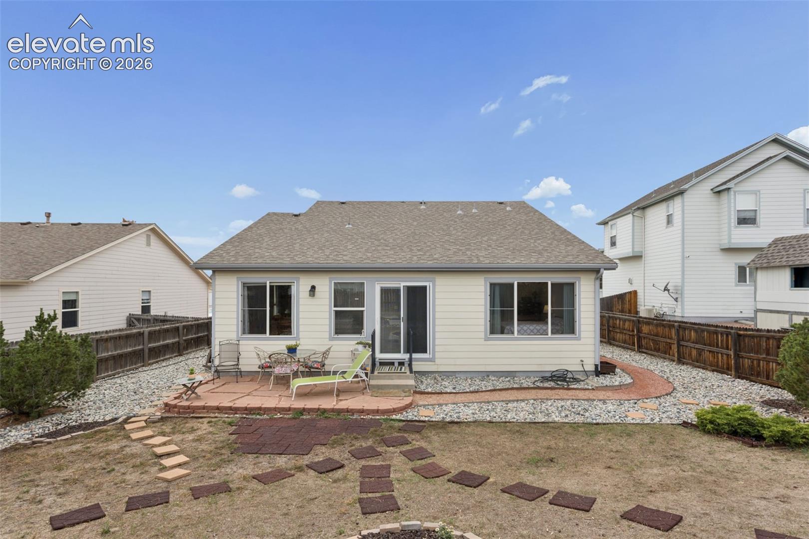 Rear exterior with a flag stone patio, slider door, multiple windows, and partial rock landscaping