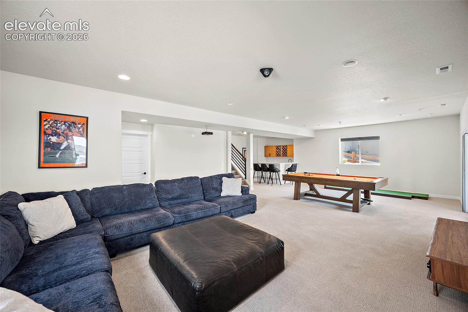 Spacious recreation room featuring recessed lighting, a built-in wet bar with wood-finish cabinetry, and a window providing natural light