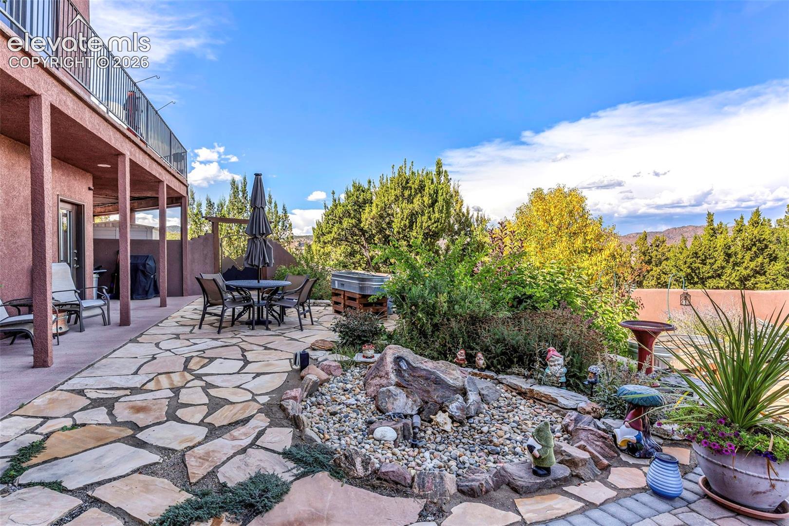 Flagstone patio featuring a rock garden, covered lower-level porch, metal railing, and mature landscaping