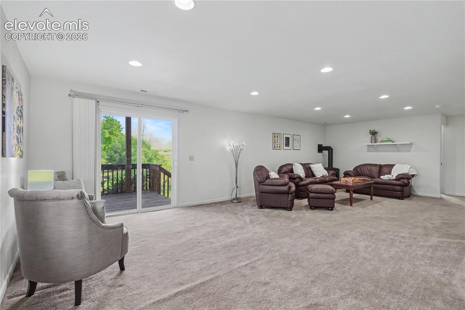 Spacious room featuring light gray carpet, recessed lighting, white walls, and a sliding glass door leading to a wooden deck
