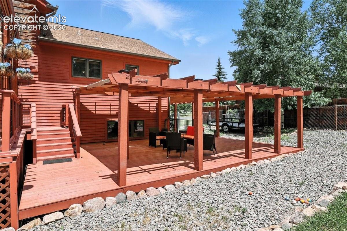 Exterior space featuring a wood-plank deck, a structural wooden pergola, and a staircase with a wooden railing
