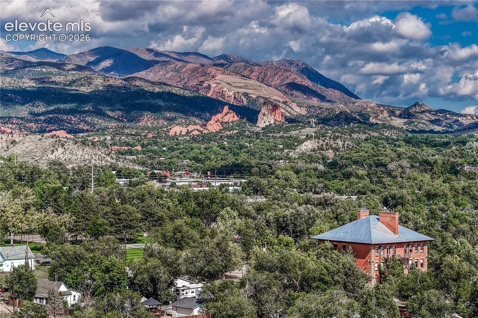 Expansive landscape featuring distant mountains, lush green trees, and a red brick building with a blue-gray roof