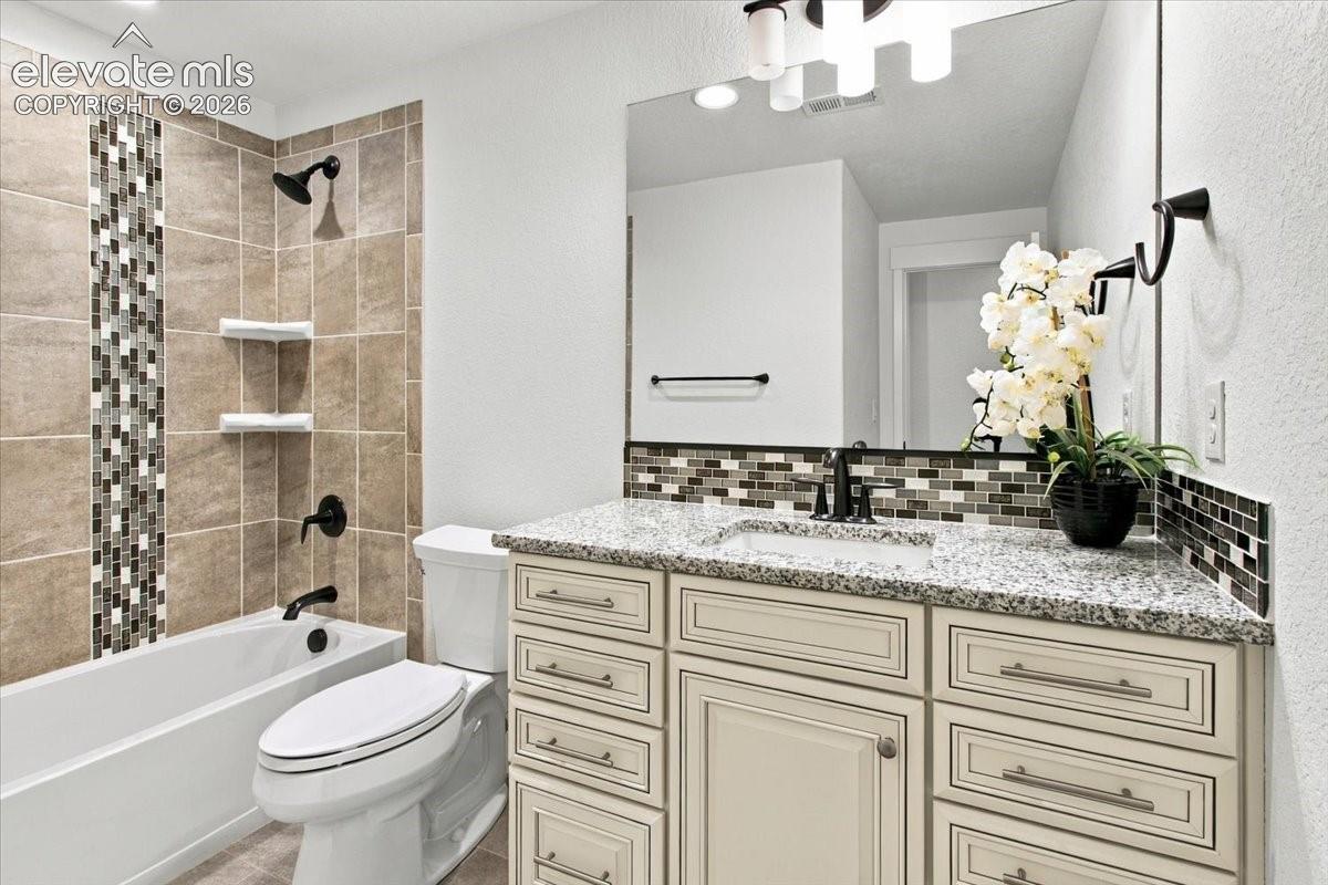 Bathroom featuring a vanity with stone-style countertop and under-mount sink, tiled shower enclosure with decorative mosaic accent inlay, matte black hardware, and an expansive wall-mounted mirror