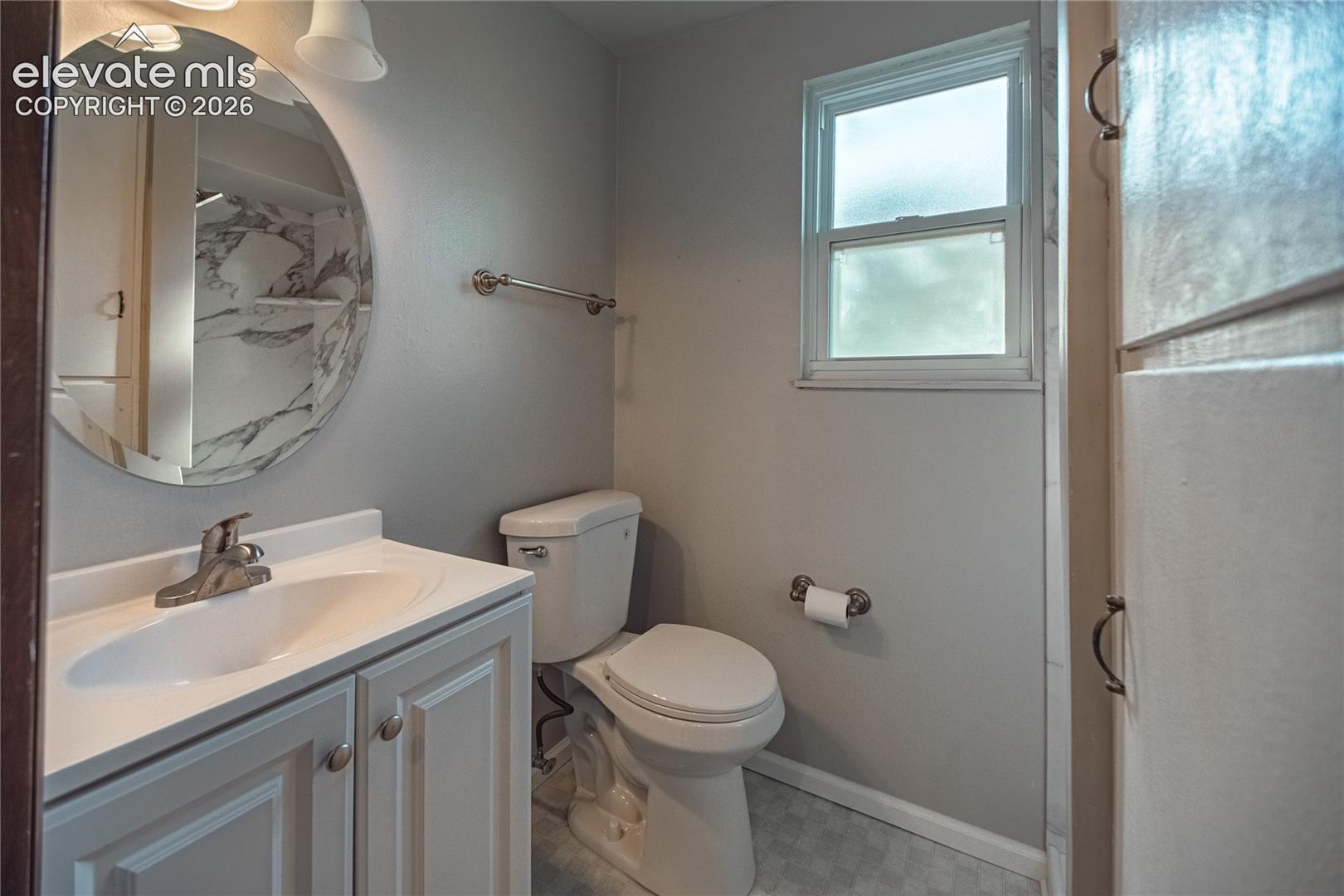Bathroom featuring a vanity with an integrated sink, round mirror, built-in cabinetry, and a window