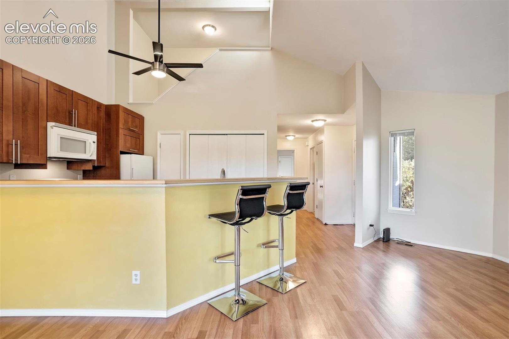 Kitchen area featuring vaulted ceilings, wood-finish cabinetry, a breakfast bar, and wood-finish flooring