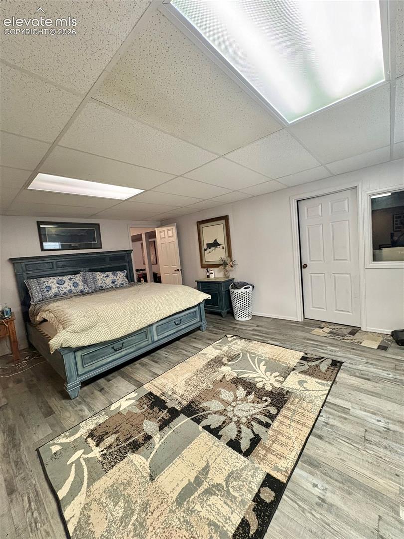 Recessed lighting, wood-finish flooring, drop ceiling, interior door with a paneled design, and a large translucent ceiling light panel