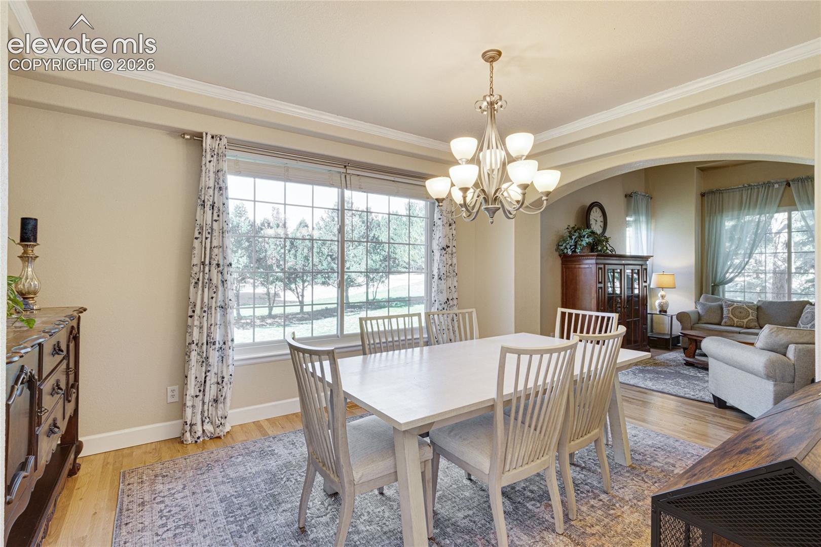 Dining area featuring wood-finish flooring, a multi-light chandelier, a large multi-pane window, and an arched architectural opening