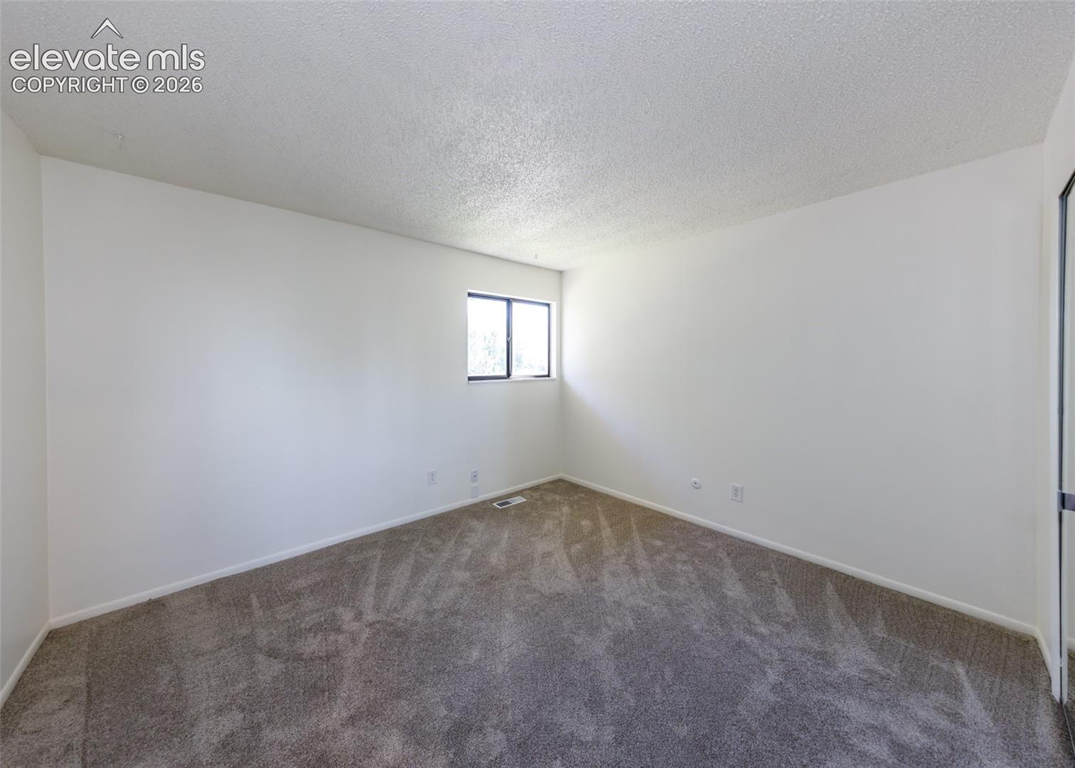 Neutral-toned carpeted flooring, textured ceiling, and a single-pane window