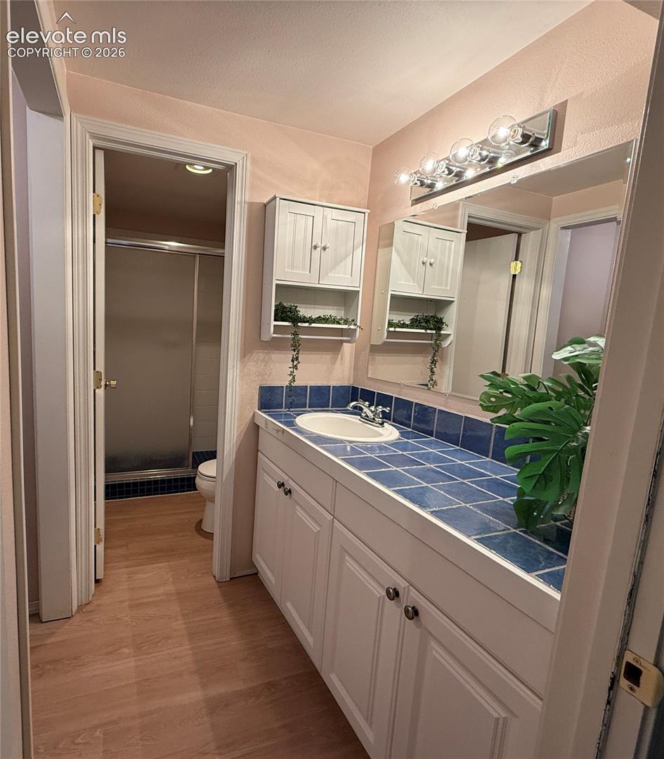 Vanity featuring a tiled countertop, sink, white shaker-style cabinetry, wall-mounted storage cabinet, and multi-bulb vanity light fixture