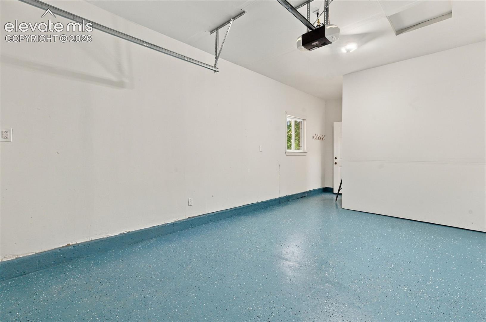 Finished garage featuring epoxy-coated flooring, painted interior walls, and an overhead automatic door opener