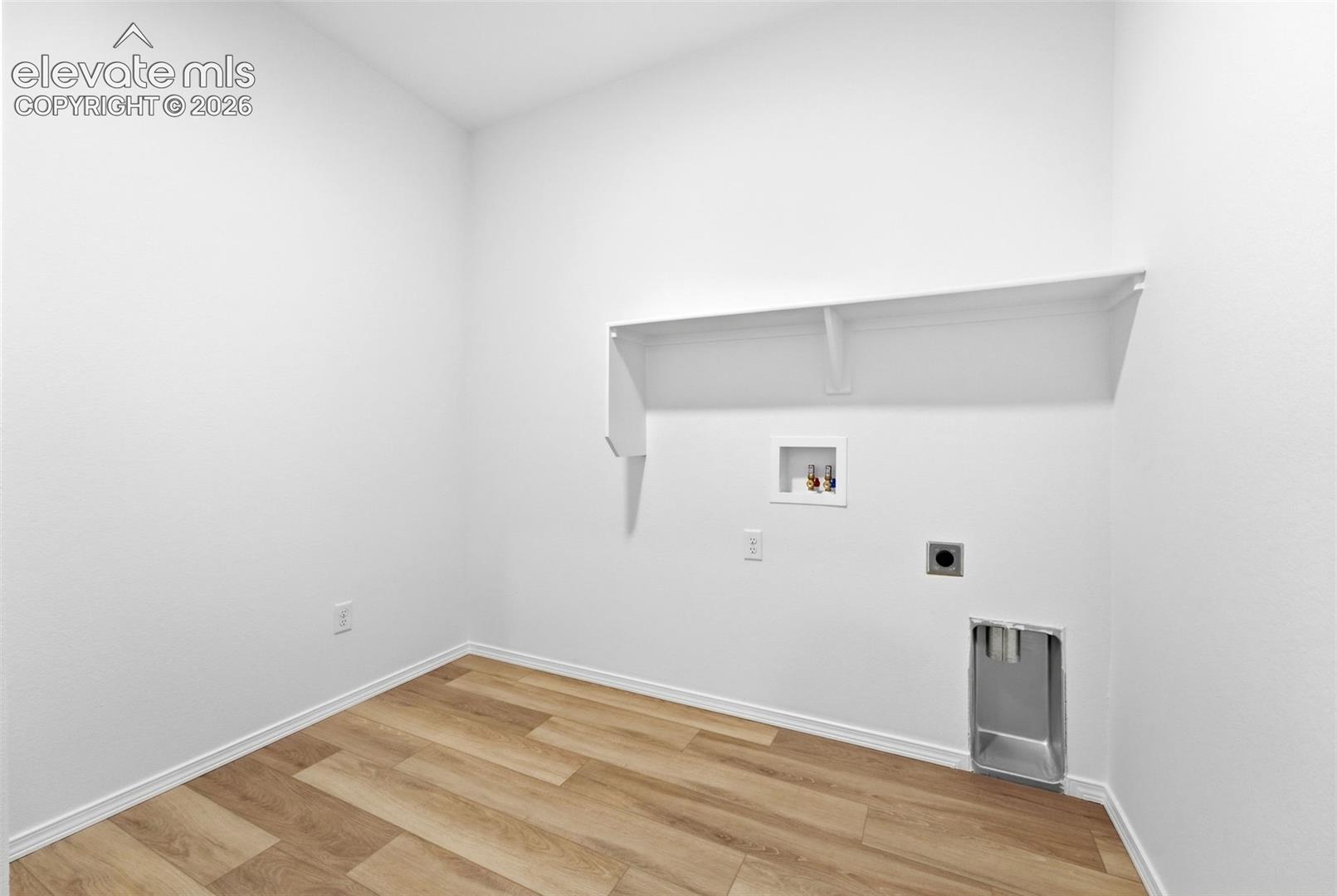 Utility space featuring wood-finish flooring, a wall-mounted shelving unit, and dedicated hookups for laundry appliances