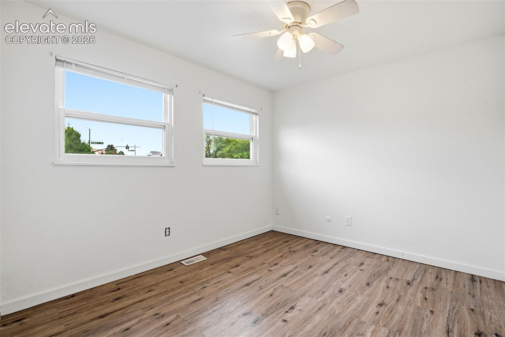 Wood-finish flooring, white walls, two windows, and a ceiling fan with integrated lighting