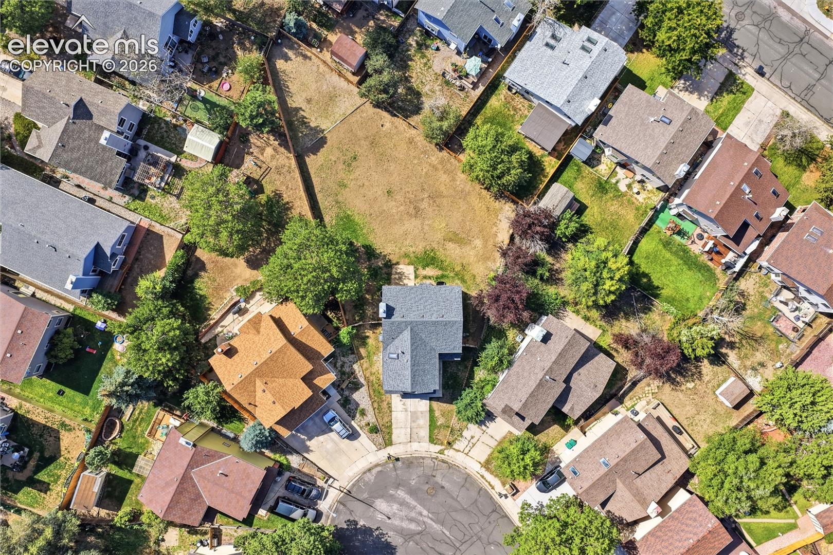 Aerial perspective of a cul-de-sac with surrounding residential properties, featuring a central property with a dark-toned roof and concrete driveway