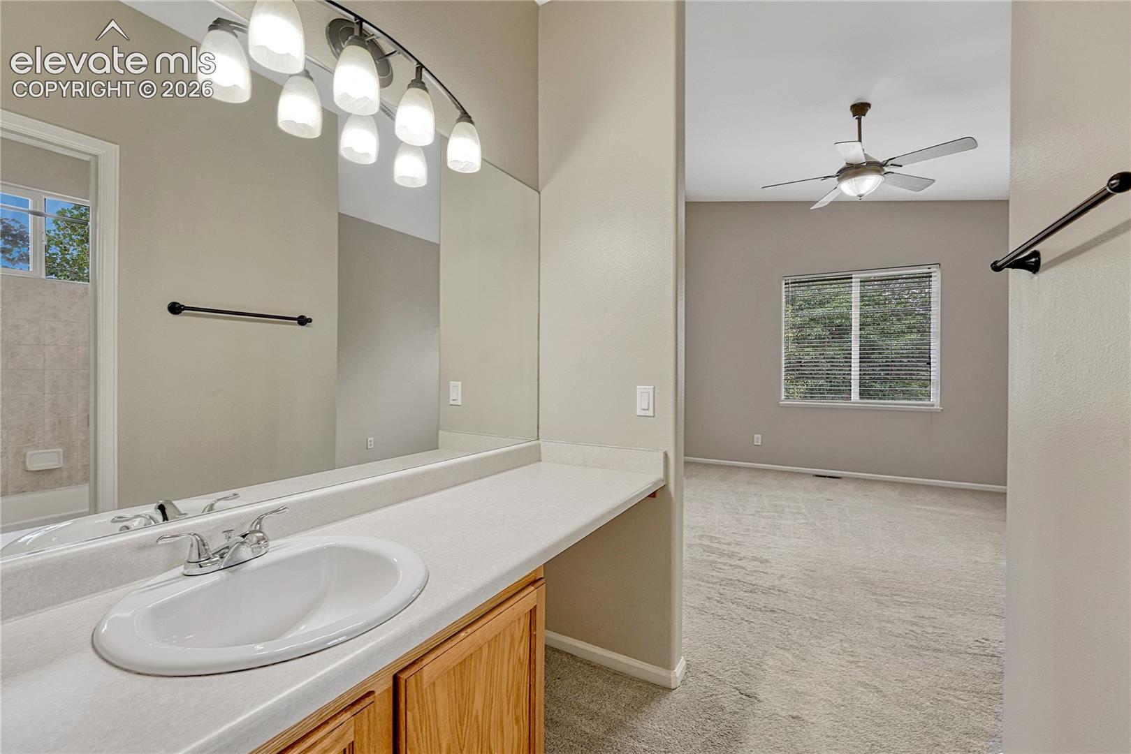 Vanity featuring wood-finish cabinetry, a white countertop with an integrated oval basin, polished chrome faucet, full-width wall mirror, and six-light fixture