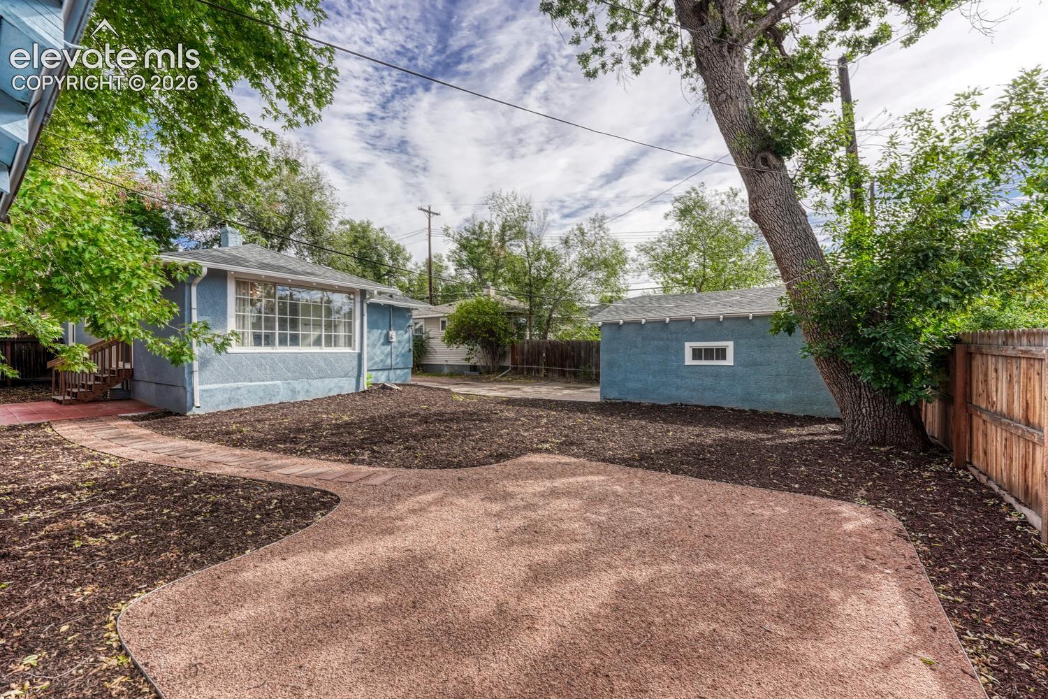 Expansive outdoor space featuring a paved patio area, mature tree, and a detached structure with a window