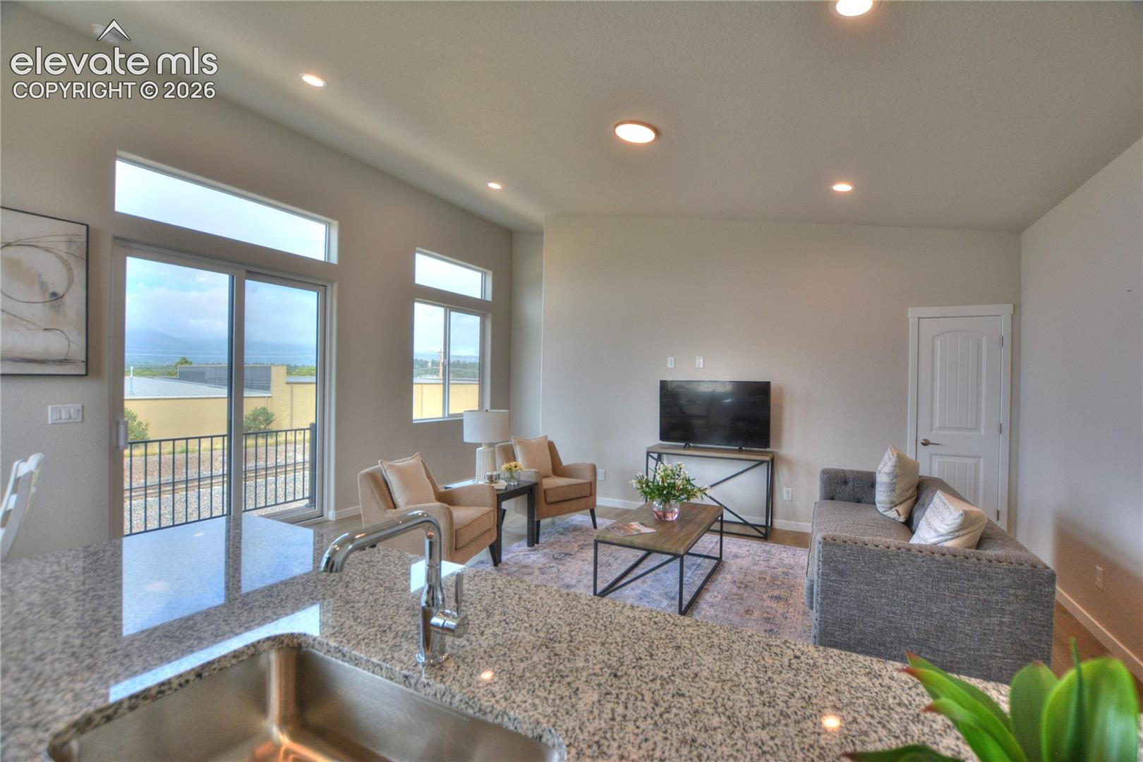 Open-concept living area featuring expansive windows with glass doors overlooking scenic vistas, recessed ceiling lighting, neutral wall finishes, wood-finish flooring, and a generously proportioned carpet defining the seating zone